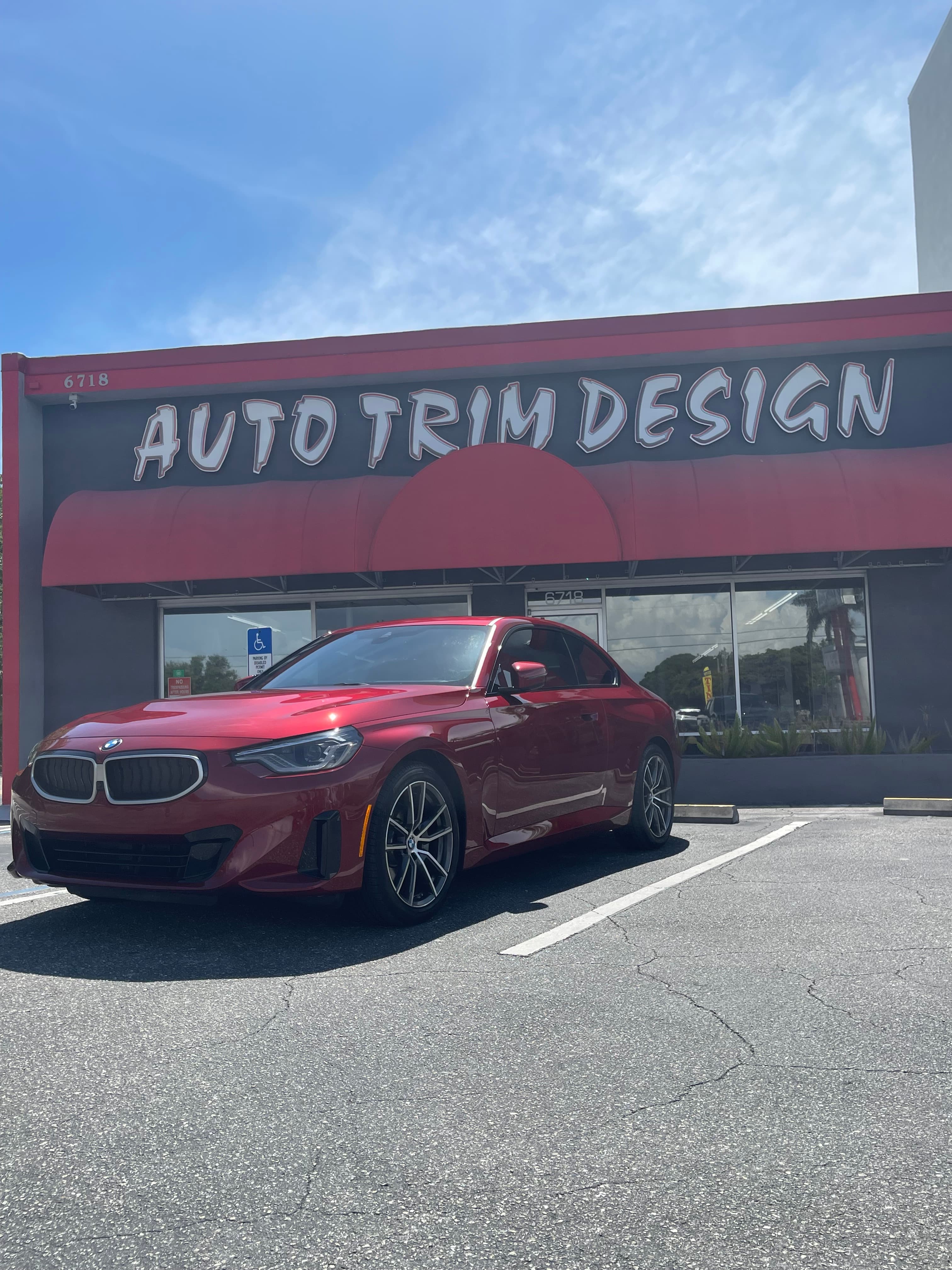 Red BMW with fresh window tint in front of Auto Trim Design shop